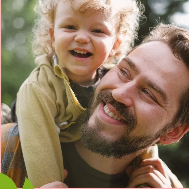 Padre sonriente con su hijo pequeño sobre los hombros, simbolizando vínculo afectivo y crianza respetuosa.