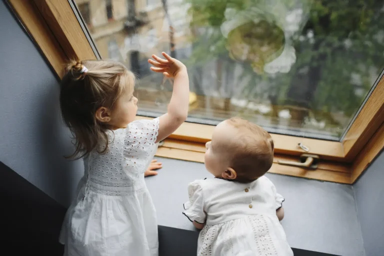 Dos niños pequeños mirando por la ventana desde casa durante el confinamiento