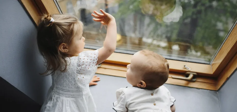 Dos niños pequeños mirando por la ventana desde casa durante el confinamiento
